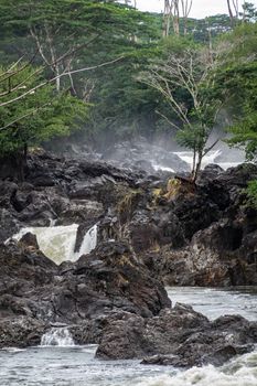 Hilo, Hawaii, USA. - January 14, 2020: Closeup of White water and lava rocks on Wailuku River surrounded by green trees and plants above Rainbow Falls.