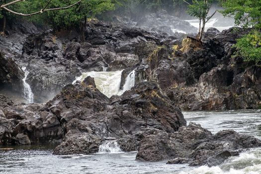 Hilo, Hawaii, USA. - January 14, 2020: Closeup of White water and lava rocks on Wailuku River surrounded by green trees and plants above Rainbow Falls.