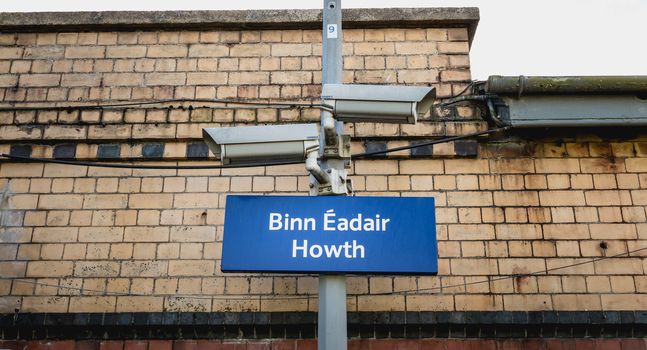 Howth, Ireland - February 15, 2019: Blue signs showing Howth train station (Bin Eadair) with platform surveillance cameras on a winter day