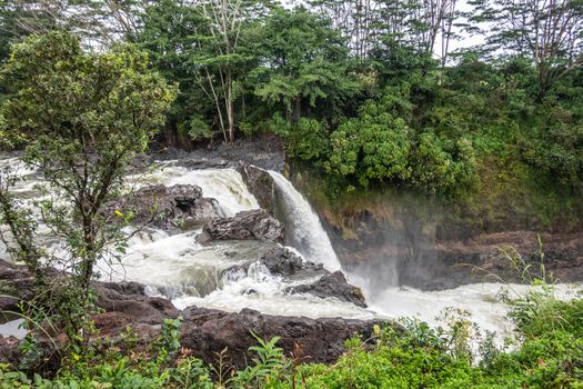 Hilo, Hawaii, USA. - January 14, 2020: White water falling over lava rocks on edge of Rainbow Falls. Green vegetation.