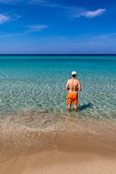 Man in the water at the sea concept of a happy holiday and freedom. Young man in the sea water on beach summer vacation, guy standing back seaside, blue sea water, holiday travel concept.