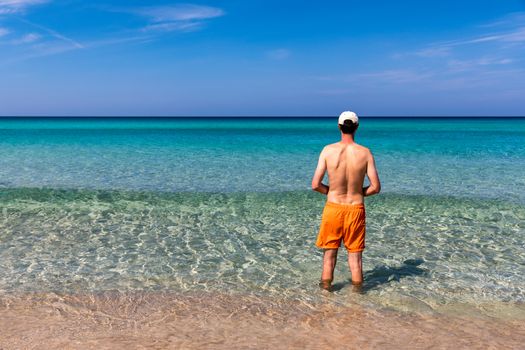 Man in the water at the sea concept of a happy holiday and freedom. Young man in the sea water on beach summer vacation, guy standing back seaside, blue sea water, holiday travel concept.