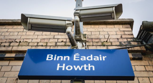 Howth, Ireland - February 15, 2019: Blue signs showing Howth train station (Bin Eadair) with platform surveillance cameras on a winter day