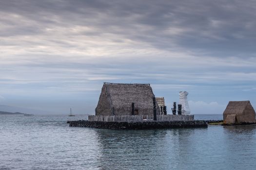 Kona, Hawaii, USA. - January 15, 2020: Kamakahonu Historic landmark. Aboriginal brown palm tree leaves huts on platform in harbor under cloudscape and floating on dark water.