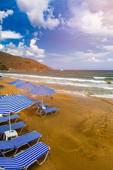 Summer vacation destination. Straw sunshades and sunbeds on the empty pebble beach with sea in the background. Vacation And Tourism Concept. Sunbeds On The Paradise Beach. Umbrellas and sunbeds.