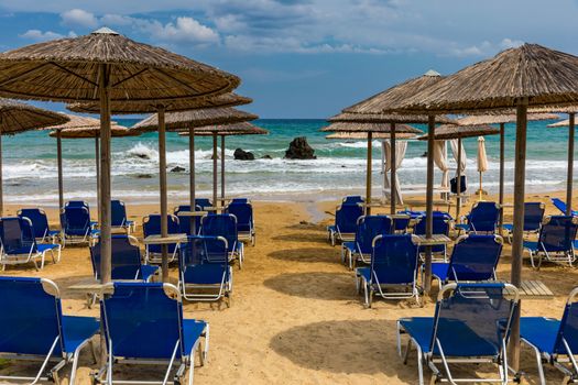 Summer vacation destination. Straw sunshades and sunbeds on the empty pebble beach with sea in the background. Vacation And Tourism Concept. Sunbeds On The Paradise Beach. Umbrellas and sunbeds.