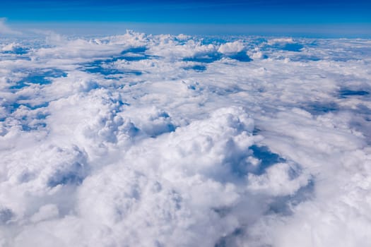 Amazing clouds and the sky as seen through the window of an aircraft. Clouds, sun, sky as seen through window of an aircraft. Bright blue sky with clouds and sunlight seen through an airplane window.