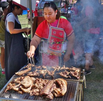 KAOHSIUNG, TAIWAN -- SEPTEMBER 29, 2018: A member of the indigenous Amis tribe in traditional costume cooks meat at the yearly harvest festival.
