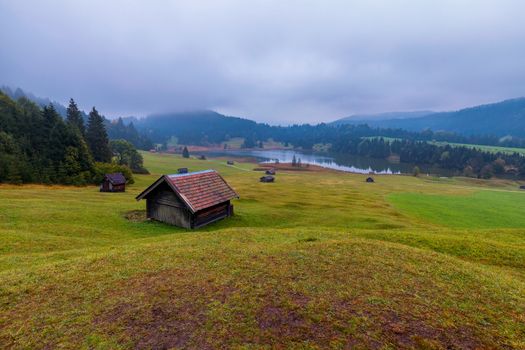 Panoramic morning scene of Wagenbruchsee (Geroldsee) lake with Zugspitze mountain range on background. Amazing autumn view of Bavarian Alps, Germany, Europe. Wooden hut on meadow by Geroldsee lake. 