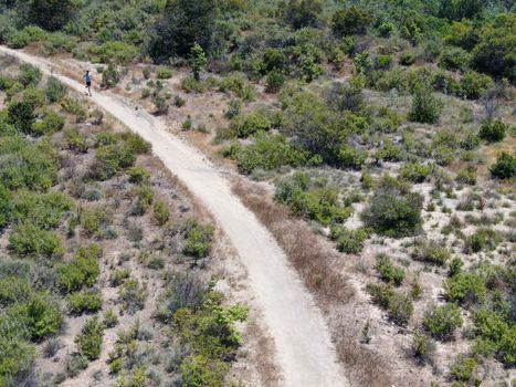 Aerial view of running man mountain bike in a small singletrack dusty trail in the valley California, USA