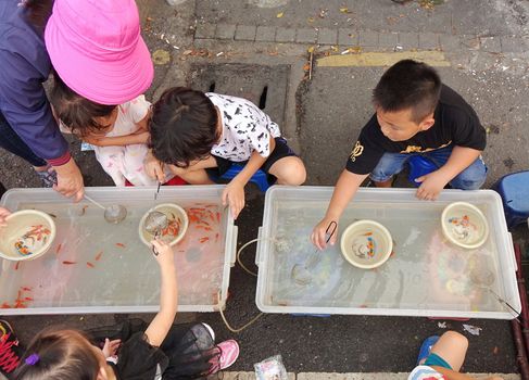KAOHSIUNG, TAIWAN -- OCTOBER 15, 2016: Young children catch small goldfish. This is a popular children's activity at outdoor markets.