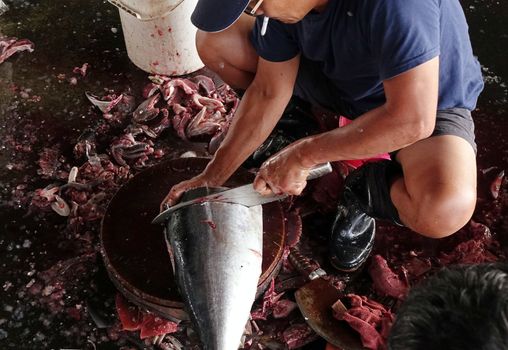 KAOHSIUNG, TAIWAN -- MAY 9, 2015: A local fishmonger cleans and slices a large tuna fish at the Sinda fishmarket.