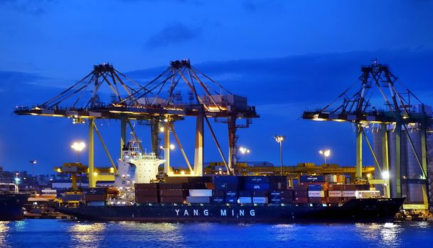 KAOHSIUNG, TAIWAN -- JUNE 2, 2019: Containers are being loaded onto ships in Kaohsiung Port at dusk