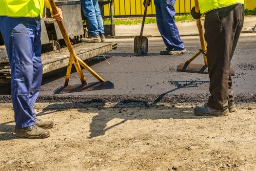 road works, workers level asphalt mix on the road with shovels