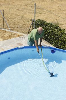 A senior man cleans up the swimming pool at his garden.