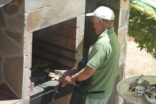 Senior man doing barbecue outdoors at beauty barbecue grill.