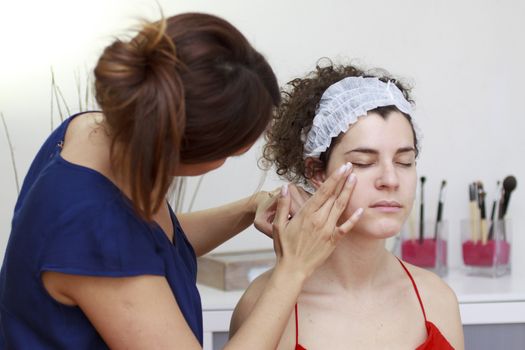 Young woman having make-up applied by a beautician.