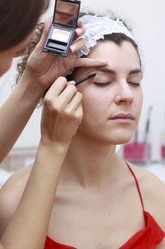 Young woman having make-up applied by a beautician.