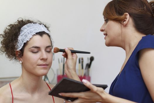 Young woman having make-up applied by a beautician.