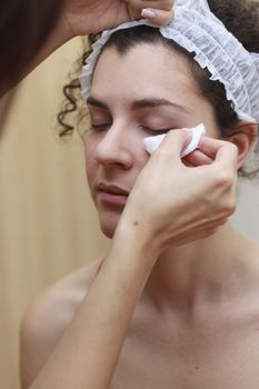 Young woman having make-up applied by a beautician.