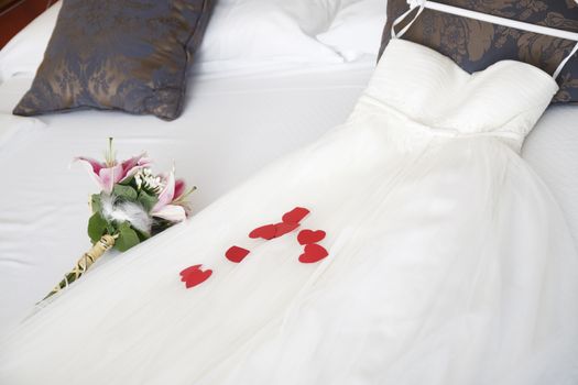 A wedding dress and a bouquet on a bed.