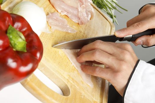 Man chopping chicken breasts on cutting board.