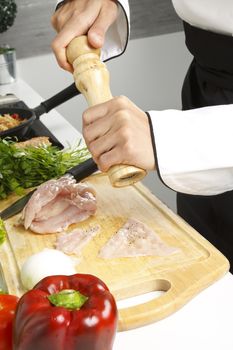 Chef adding black pepper to chicken breast.