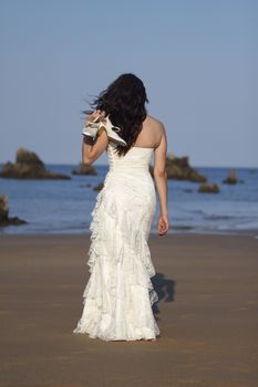Bride walking in the beach with shoes in hand.