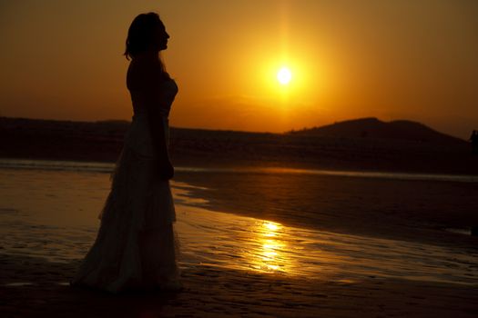 Bride contemplating beach at sunset. Low light