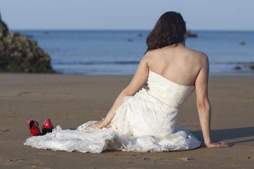 Bride sit in the beach with red shoes next to her.