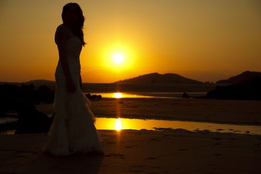 Bride contemplating beach at sunset. Low light