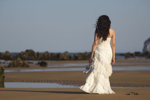 Bride walking in the beach with shoes in hand.