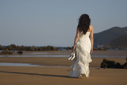 Bride walking in the beach with shoes in hand.