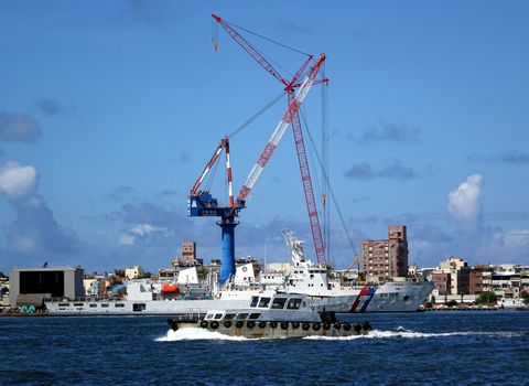 KAOHSIUNG, TAIWAN -- JULY 11, 2014: A  partial view of Kaohsiung port with large cranes and a harbor patrol boat passing by.