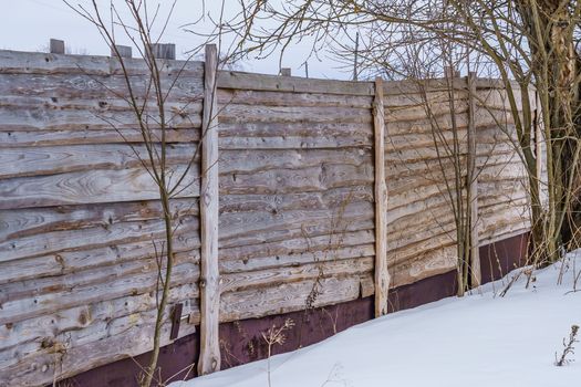 fence around the garden of unpainted boards on a winter day