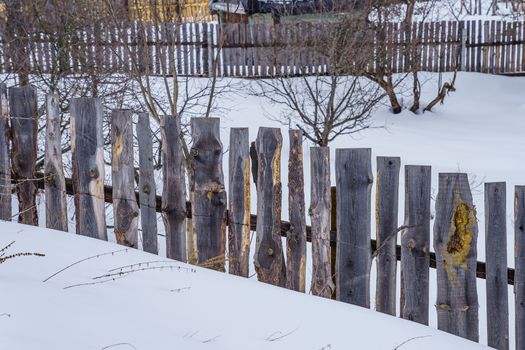 fence around the garden of unpainted boards on a winter day