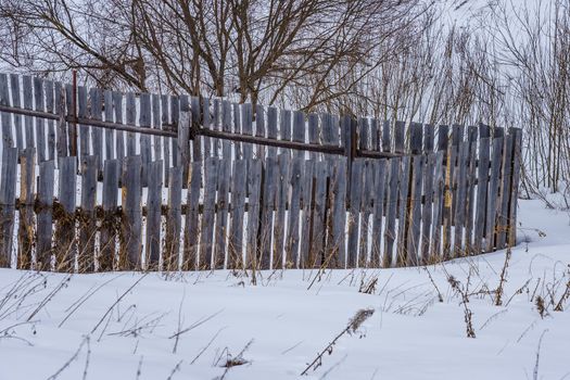 fence around the garden of unpainted boards on a winter day