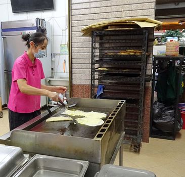 KAOHSIUNG, TAIWAN -- JUNE 9, 2016: A female chef at a traditional Chinese breakfast shop prepares fried pancakes with egg and scallions.
