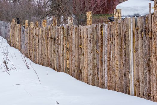 fence around the garden of unpainted boards on a winter day