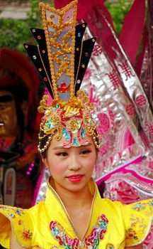 KAOHSIUNG, TAIWAN -- AUGUST 15, 2015: A beautiful female dancer with an elaborate headgear and yellow costume awaits her turn at the outdoor Third Prince temple carnival.