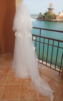 Female bride in lace wedding dress stood on balcony looking to sea of tropical ocean coastal resort