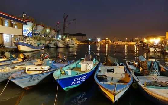 KAOHSIUNG, TAIWAN -- DECEMBER 22, 2018: A small fishing harbor by night on the island of Qijin. In the back are colorful fuel storage tanks.
