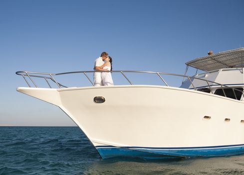 Young newly married couple kissing on the front of a private yacht