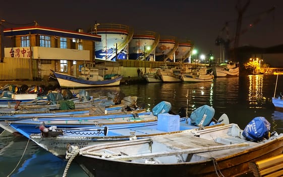 KAOHSIUNG, TAIWAN -- DECEMBER 22, 2018: A small fishing harbor by night on the island of Qijin. In the back are colorful fuel storage tanks.