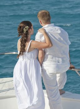 Newly married couple embracing while stood on the bow of a boat