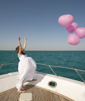 Newly married bride releasing a bunch of balloons while standing on the front of a boat