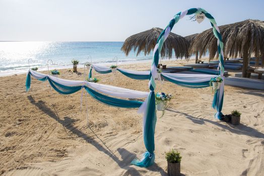 Setup of wedding day marriage aisle with drapes and arch on sandy tropical beach paradise to open ocean background 