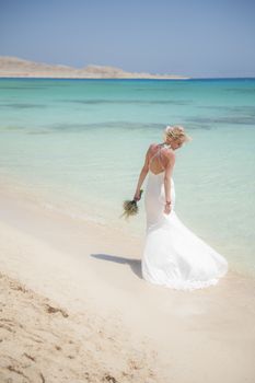 Beautiful woman bride at a tropical beach paradise on wedding day in white gown dress with ocean view