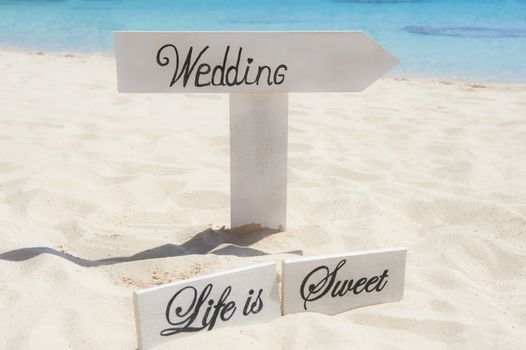 Tropical island beach wedding ceremony setup with signpost and ocean background