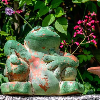 Pretty green potted frog sitting on a wall in front of flowers